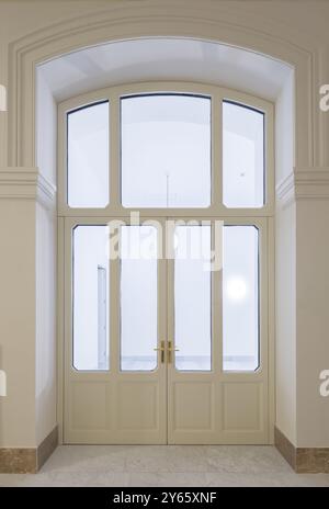 Un'elegante porta in legno con pannelli di vetro collocata in un sofisticato ingresso per uffici, caratterizzata da architettura ad arco e pavimento in marmo chiaro. Foto Stock