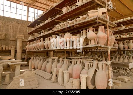 Un deposito di antiche ceramiche e manufatti conservati a Pompei, che espone una varietà di urne, anfore e colonne sotto un magazzino protetto Foto Stock