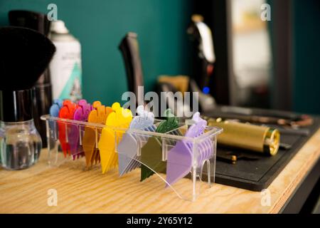 Clip per capelli colorate e strumenti da barbiere professionali, tra cui spazzola e regolacapelli, disposti in modo ordinato su una superficie di legno in un barbiere, che evocano un cle Foto Stock