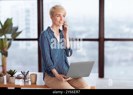 Donna Imprenditore Che Parla Su Cellphone Seduta Sulla Scrivania In Ufficio Foto Stock