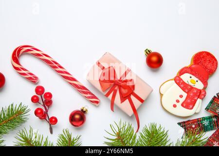 Composizione piatta con decorazioni natalizie, scatola regalo e deliziosi biscotti a forma di pupazzo di neve su sfondo bianco Foto Stock