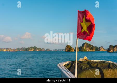 La bandiera rossa del Vietnam ondeggia su una barca che naviga attraverso il punto di riferimento della Baia di ha Long, un popolare luogo turistico. Concetto di turismo in Vietnam e Sud Est Foto Stock