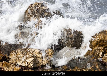 Pietre di frangiflutti costiere testurizzate, con una spruzzata del mare ionico. Giornata di sole. Astrakeri, Corfù settentrionale, Grecia. Foto Stock