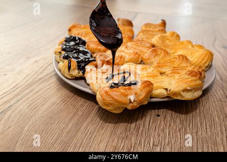 Una donna versa cioccolata calda sugli eclari usando un cucchiaio. Foto Stock