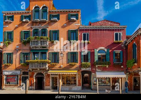 Un uomo cammina con il suo cane davanti a edifici colorati e negozi lungo fondamenta Manin sul canale Rio dei vetrai sull'isola di Murano, vicino a Venezia, in Italia Foto Stock