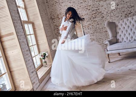 Mi sento felice. L'intera lunghezza di una giovane donna attraente in accappatoio di seta che prova il suo abito da sposa mentre balla in camerino Foto Stock