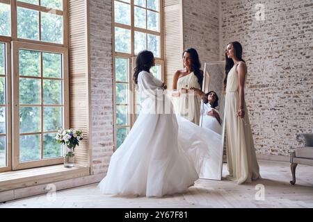 Stupita dalla bellezza delle spose. Due giovani donne attraenti sorridenti mentre guardano la sposa nel camerino Foto Stock