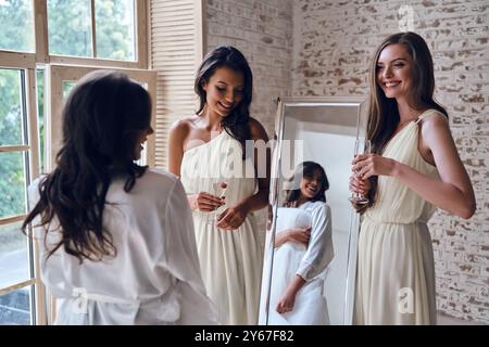 Si adatta perfettamente. Due giovani donne attraenti sorridenti mentre guardano la sposa nel camerino Foto Stock