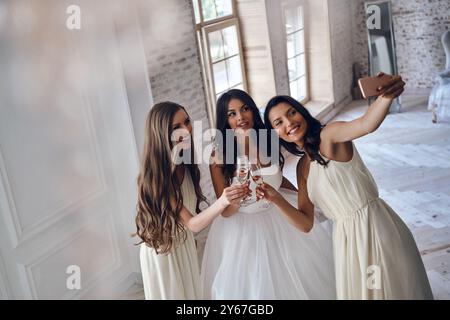 Cattura momenti felici. Vista dall'alto dell'attraente giovane sposa che si unisce alle sue bellissime damigelle mentre scattano selfie in camerino Foto Stock