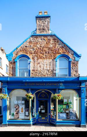 Immagine di testa della North Berwick's Pharmacy, un negozio di chimici locali dipinto di blu e un edificio in mattoni sulla High Street, in una mattinata di cielo limpido Foto Stock