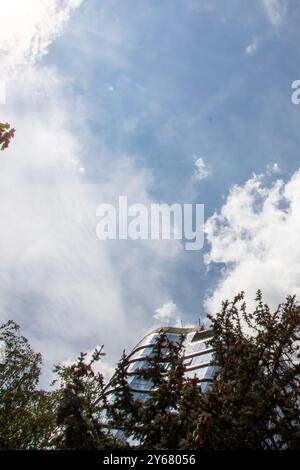 Esiste un vasto cielo blu adornato da soffici nuvole bianche, e in primo piano, ci sono alberi lussureggianti che ondeggiano dolcemente nella brezza Foto Stock