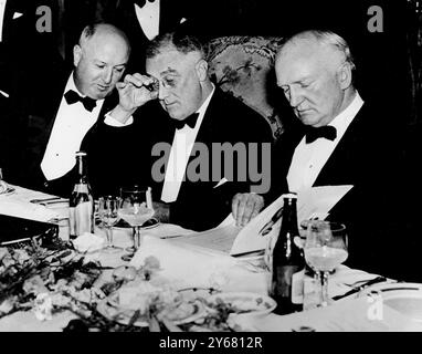 Il presidente Franklin D Roosevelt sbircia attraverso i suoi occhiali al menu con il Postmaster General James A Farley (a sinistra) e Joseph P. Tumulty. Al Democratic Victory Dinner all'Hotel Mayflower di Washington. 15 marzo 1937 Foto Stock