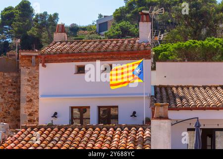 Vista delle tradizionali case in pietra con tetti piastrellati a Tossa de Mar, Catalogna, Spagna, sullo sfondo della bandiera nazionale e del cielo azzurro. Foto Stock