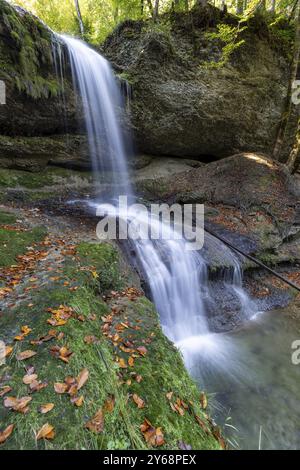 Una cascata alta e stretta si estende su rocce coperte di muschio, circondate da foglie autunnali nella foresta, Hasenreuter Wasserfall, Scheidegg, Baviera, germe Foto Stock