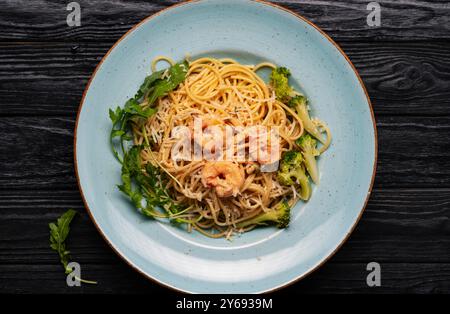 Spaghetti italiani con gamberi e salsa di pomodoro in un piatto su un tavolo di legno nero, vista dall'alto, cucina italiana Foto Stock