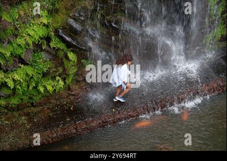 Donna che passa sotto una cascata nei giardini del palazzo monte, circondata da una vegetazione lussureggiante Foto Stock