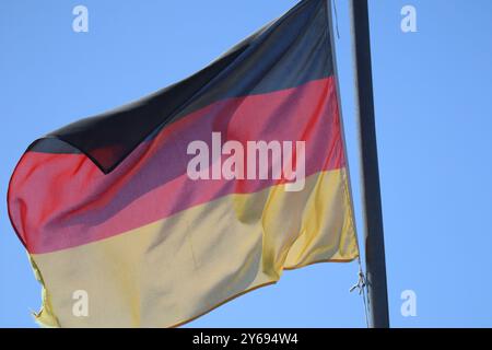 Bandiera tedesca che sventola al vento. Sventolando la bandiera della Germania sull'asta di bandiera contro il cielo blu. Germania. Colori nero, rosso e giallo sulla bandiera tedesca in A. Foto Stock