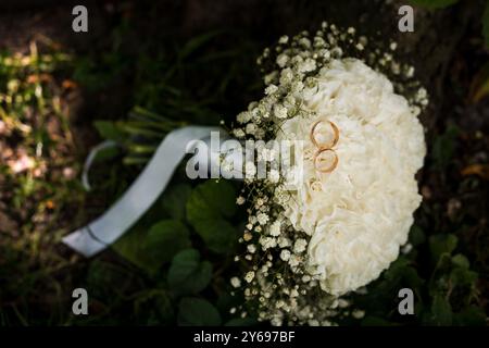 Elegante bouquet nuziale adornato da anelli dorati che riposano su una lussureggiante erba verde. Foto Stock