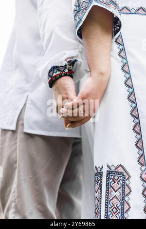 Intimo legame: Le mani di una coppia si stringono in un abbigliamento tradizionale culturale con un elegante ricamo. Foto Stock
