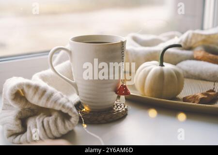 Accogliente allestimento autunnale con una tazza di tè fumante e arredi per la casa Foto Stock