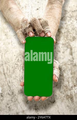 Le mani della mamma hanno delle bende sporche. Mamma, diavolo, male, satana, o zombie mani che tengono i telefoni cellulari o cellulari con schermi verdi con un gru Foto Stock