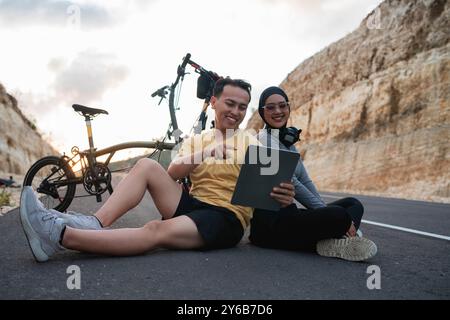 motociclista maschile che usa il tablet e mostra un amico hijab Foto Stock