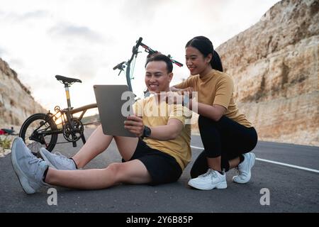 ciclista di sesso femminile e maschile seduto e che utilizza un tablet digitale Foto Stock