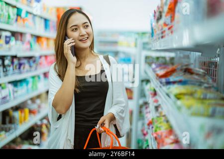 la donna asiatica riceve una chiamata mentre fa shopping portando il carrello della spesa al minimarket Foto Stock