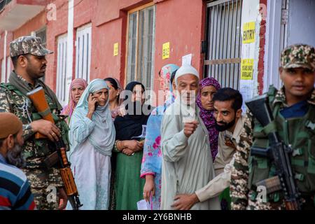 I soldati paramilitari indiani sono in guardia mentre gli elettori del Kashmir aspettano in coda per votare fuori dal seggio elettorale durante la seconda fase delle elezioni dell'assemblea del Jammu e del Kashmir nella periferia di Srinagar. Queste sono le prime elezioni dell'assemblea locale in un decennio e le prime da quando nuova Delhi ha revocato lo status semi-autonomo della regione nel 2019, ponendola sotto il dominio diretto. Quasi nove milioni di persone sono registrate per votare nella regione contesa, tradizionalmente nota per i boicottaggi contro il governo indiano. Foto Stock