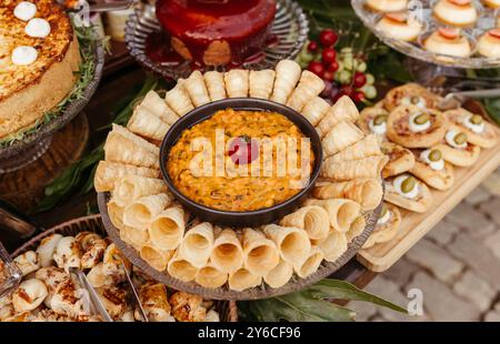 Un delizioso assortimento di vari antipasti, tra cui una ciotola di immersione circondata da dolci, formaggi e altri stuzzichini su un tavolo di legno. Foto Stock
