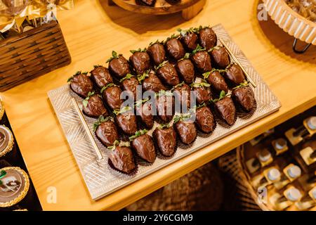 Un vassoio di deliziose fragole ricoperte di cioccolato esposto su un tavolo di legno, perfetto per dessert o per un'occasione speciale. Foto Stock