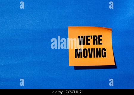 Stiamo spostando il messaggio scritto su carta arancione con sfondo blu. Concettuale stiamo spostando il simbolo. Copia spazio. Foto Stock
