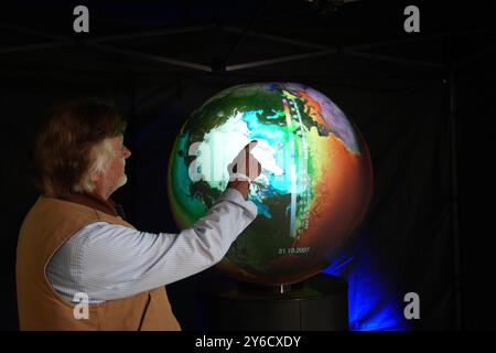 Amburgo, Germania. 25 settembre 2024. Arved Fuchs, esploratore polare e avventuriero, punta a Bear Island nell'Oceano Artico, la destinazione della sua ultima spedizione, su un globo digitale che visualizza le temperature della superficie del mare in uno stand durante il 14° Extreme Weather Congress presso la HafenCity University di Amburgo. Uno degli obiettivi del congresso di tre giorni è il tema del clima estremo nel cambiamento climatico. Crediti: Marcus Brandt/dpa/Alamy Live News Foto Stock