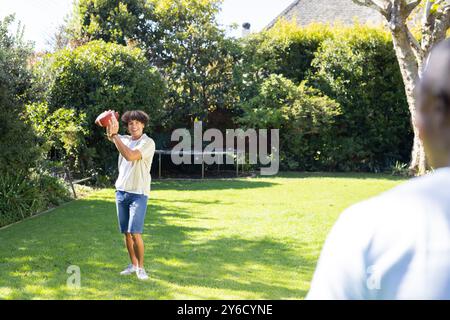 All'aperto, giocando a pesca, un giovane che lancia il calcio ad un amico in cortile Foto Stock