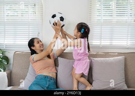 Madre e figlia giocano con la palla di calcio sul divano nel luminoso soggiorno Foto Stock