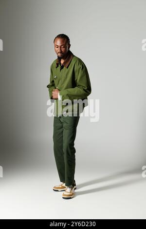 Un giovane uomo elegante vestito di verde mette in posa su uno sfondo grigio. Foto Stock