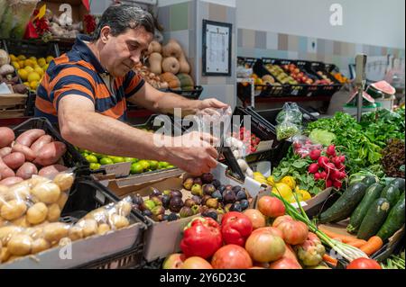 Sesimbra, Portogallo - 10 settembre 2024: L'uomo ispeziona varie verdure e frutta fresche in un vivace contesto di mercato. Foto Stock