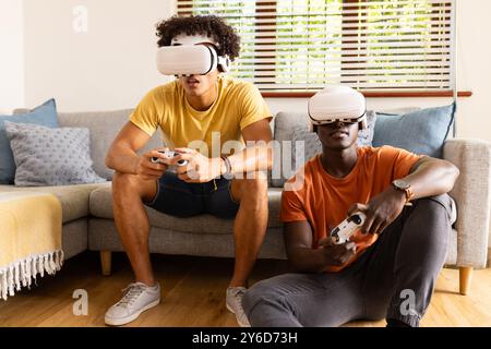 A casa, giocando ai videogiochi, due diversi amici maschi che indossano occhiali VR e controllori di tenuta Foto Stock