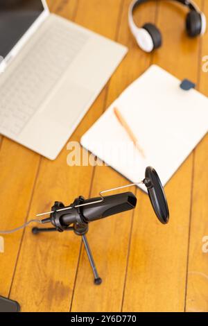 A casa, configurazione Podcasting con microfono, laptop, cuffie e blocco note su un tavolo in legno Foto Stock