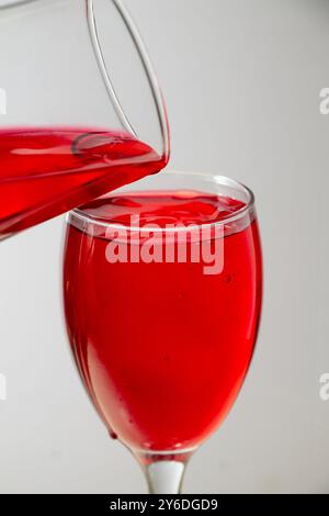 primo piano di due bicchieri liquidi rossi riempiti di liquido rosso che vengono versati sopra di essi. Foto Stock