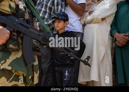 Un ragazzo del Kashmir guarda al passato soldato paramilitare indiano si mette in guardia mentre gli elettori aspettano in coda per votare fuori dal seggio elettorale durante la seconda fase delle elezioni dell'assemblea del Jammu e del Kashmir a Budgam, a sud-ovest di Srinagar. Queste sono le prime elezioni dell'assemblea locale in un decennio e le prime da quando nuova Delhi ha revocato lo status semi-autonomo della regione nel 2019, ponendola sotto il dominio diretto. Quasi nove milioni di persone sono registrate per votare nella regione contesa, tradizionalmente nota per i boicottaggi contro il governo indiano. Foto Stock