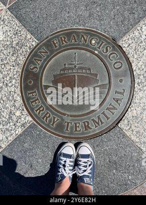 Piedi in scarpe Converse con una targa in metallo al terminal dei traghetti. Foto Stock