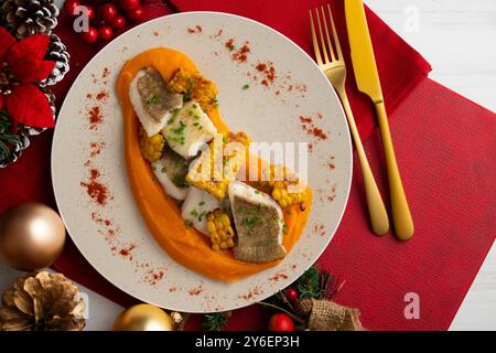 Delizioso pesce sogliola con crema di carote e mais. Tavolo con vista dall'alto e decorazioni natalizie. Foto Stock