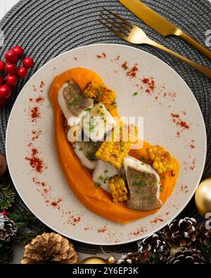 Delizioso pesce sogliola con crema di carote e mais. Tavolo con vista dall'alto e decorazioni natalizie. Foto Stock