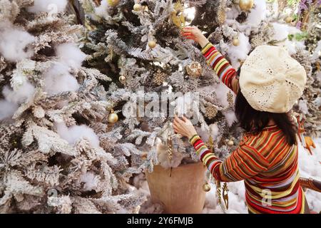 Mani femminili che decorano l'albero di Natale con un ornamento a forma di fiocco di neve scintillante Foto Stock
