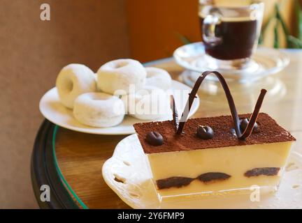 Primo piano del Tiramisu italiano con ciambelle sfocate e caffè nero sullo sfondo Foto Stock