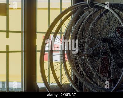 Ruote per biciclette d'epoca in un'accogliente officina di riparazione, appoggiate su una finestra illuminata dal sole, in attesa dell'attenzione di un esperto Foto Stock