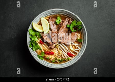 Zuppa vietnamita Pho Bo, ciotola di zuppa asiatica fresca con spaghetti di riso, carne di manzo, erbe, germogli di soia e peperoncino su sfondo nero, vista dall'alto. asi fatto in casa Foto Stock