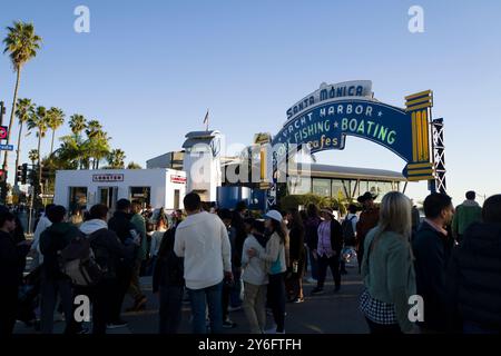 La folla si riunisce sotto il cartello del porto degli yacht di Santa Monica, godendosi una giornata di ristoranti all'aperto, pesca sportiva e nautica lungo il pittoresco lungomare. Foto Stock