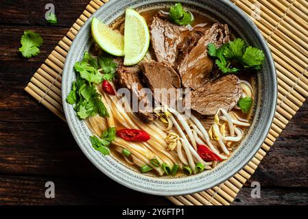 Zuppa vietnamita Pho Bo, ciotola di zuppa asiatica fresca con spaghetti di riso, carne di manzo, erbe, germogli di soia e peperoncino su sfondo di legno, vista dall'alto. Cuisi asiatici Foto Stock